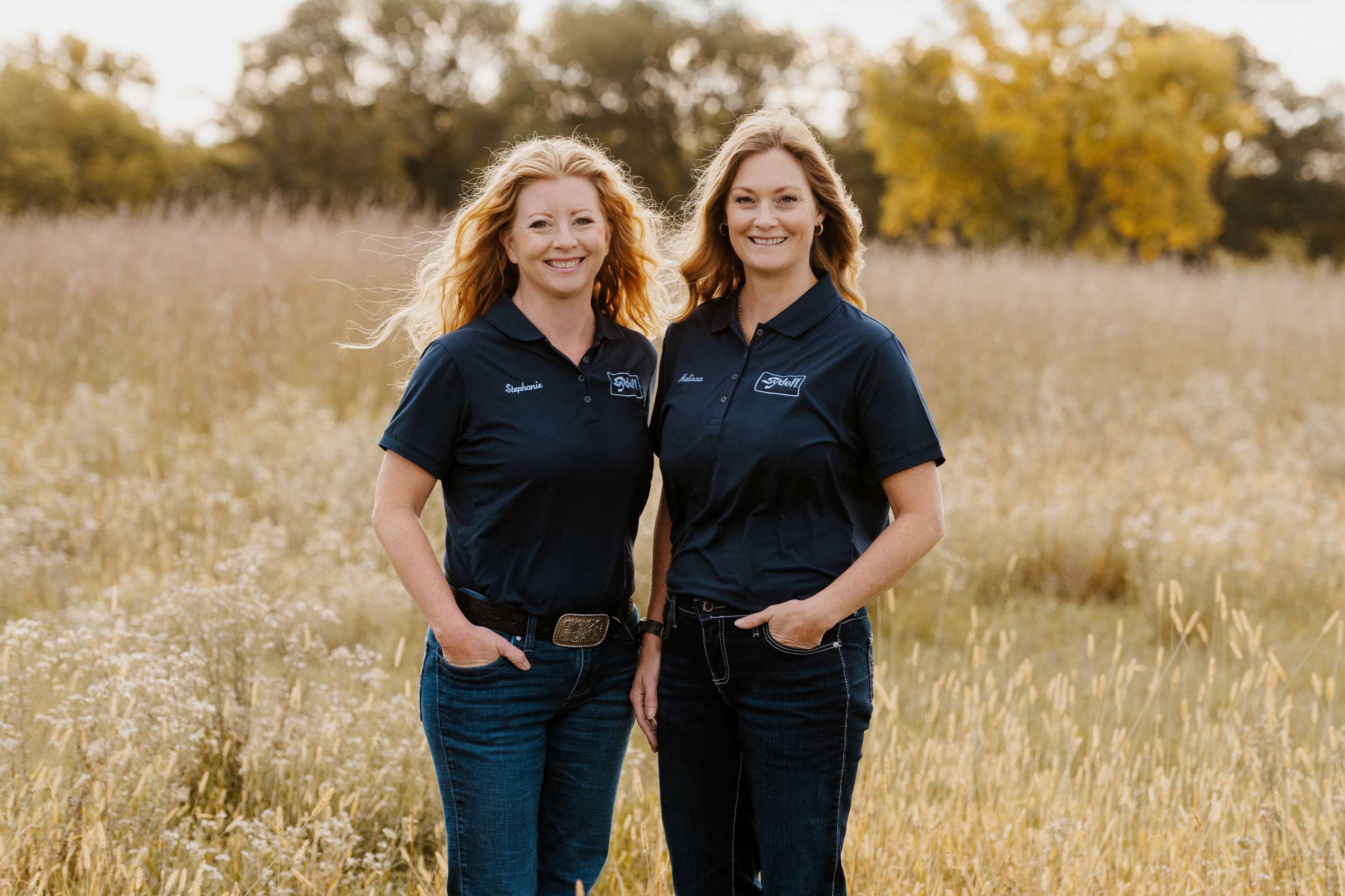 Two women in matching Sydell blue shirts standing in a field
