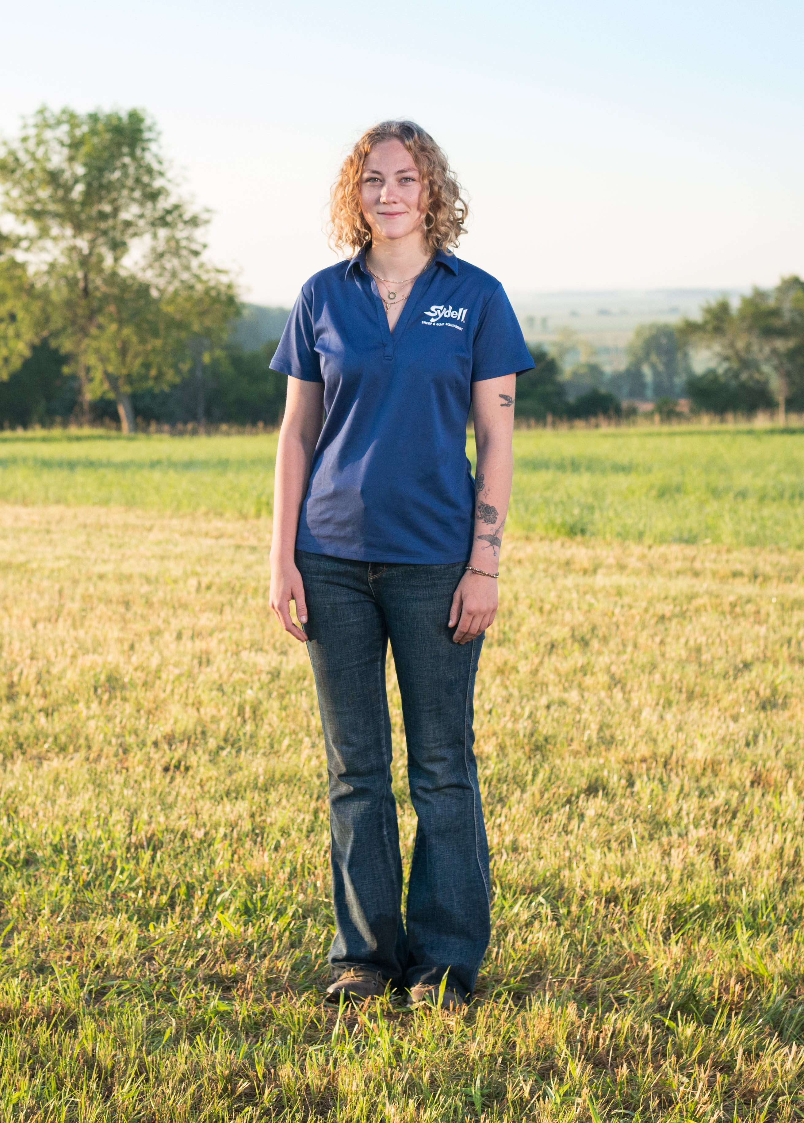 Person wearing a blue shirt with a Sydell logo standing in a field