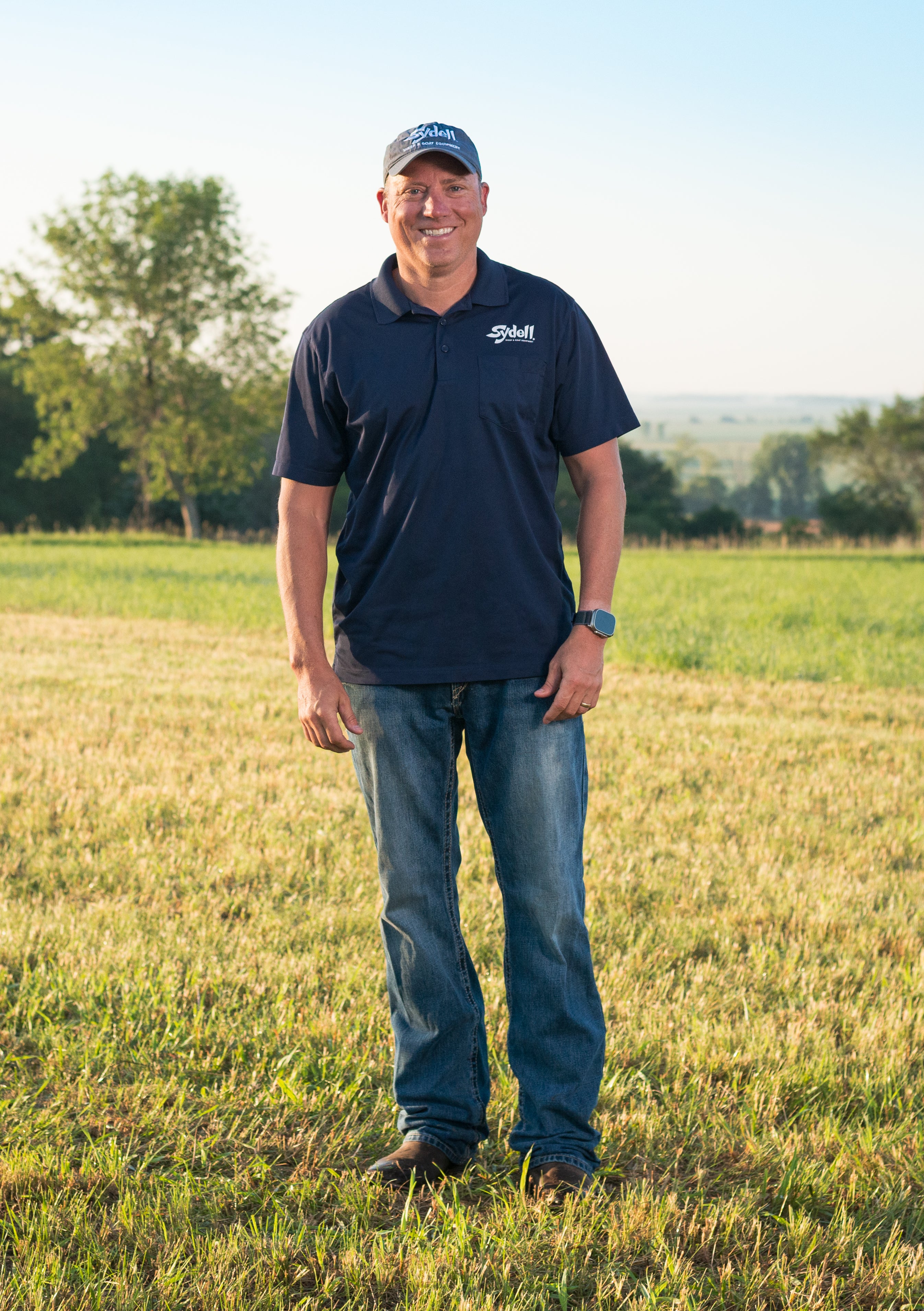 Person wearing a blue shirt with a Sydell logo standing in a field